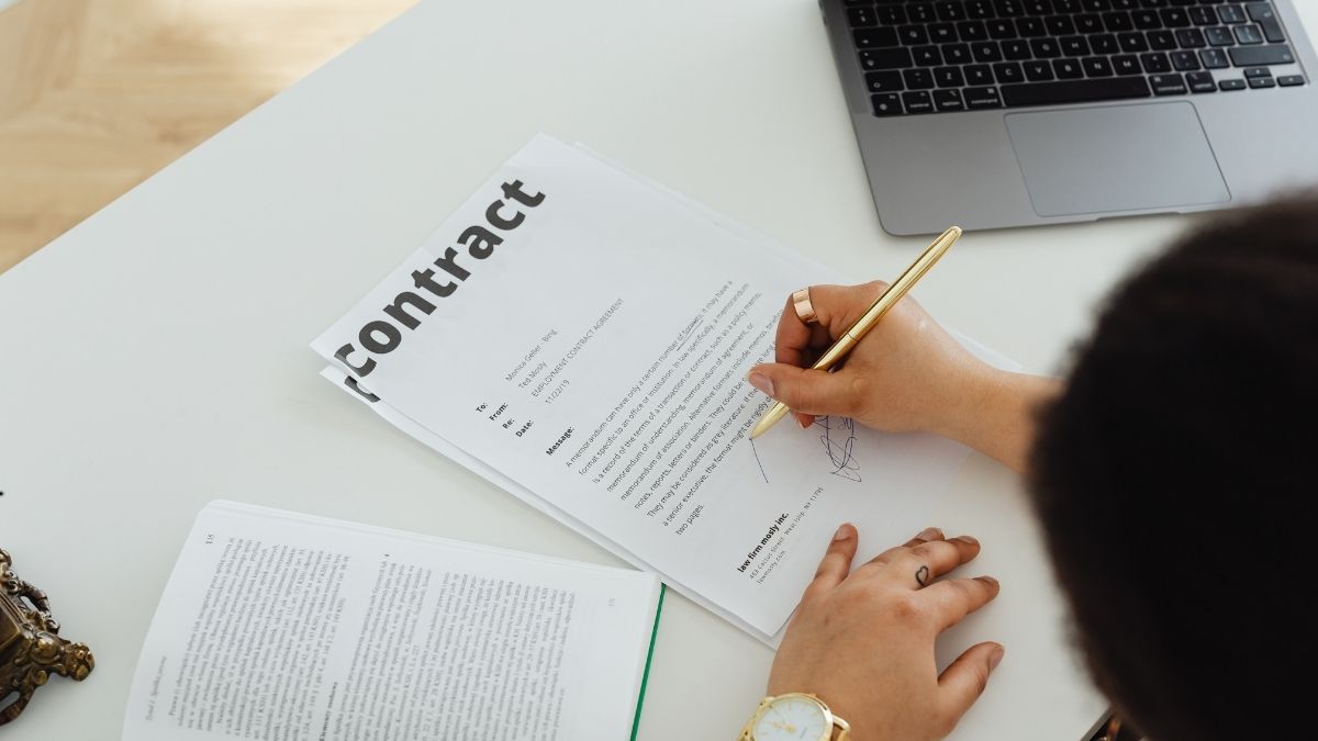 Een contract op een witte tafel. Een persoon met gouden ring en gouden horloge ondertekent het contract met een gouden pen.